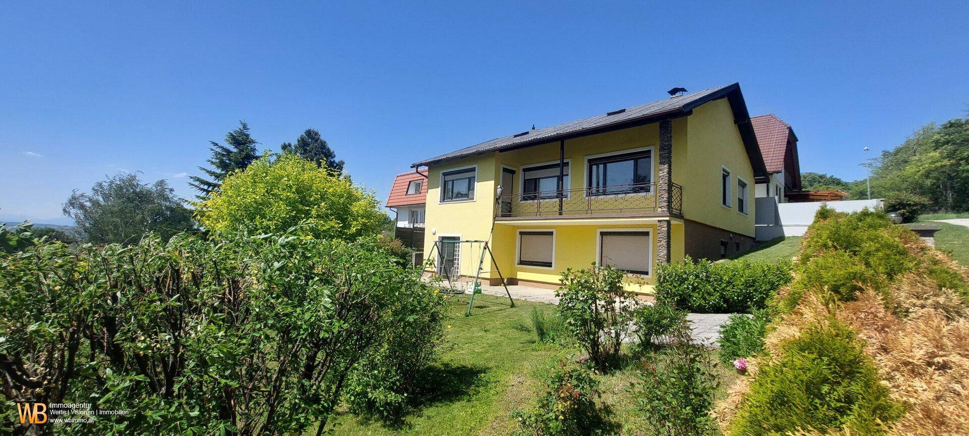 Ansicht des gelben Hauses von der Gartenseite, umgeben von viel Grün.