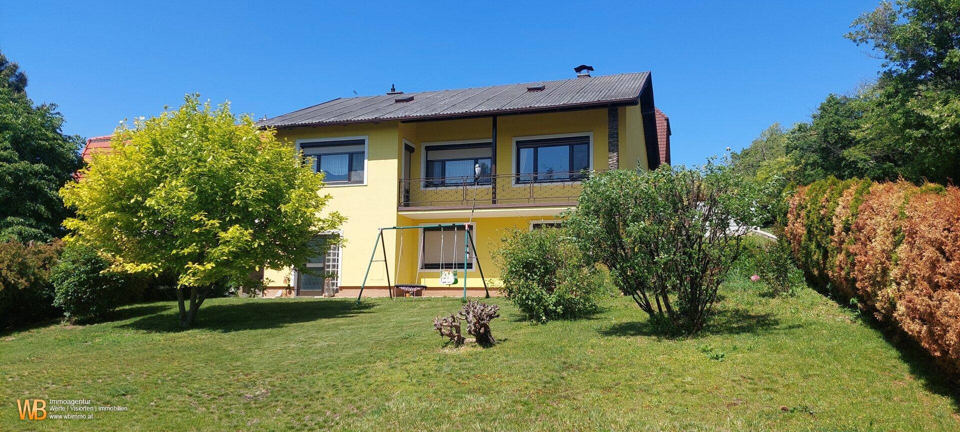 Gelbes Einfamilienhaus mit großem Garten und Spielbereich für Kinder.