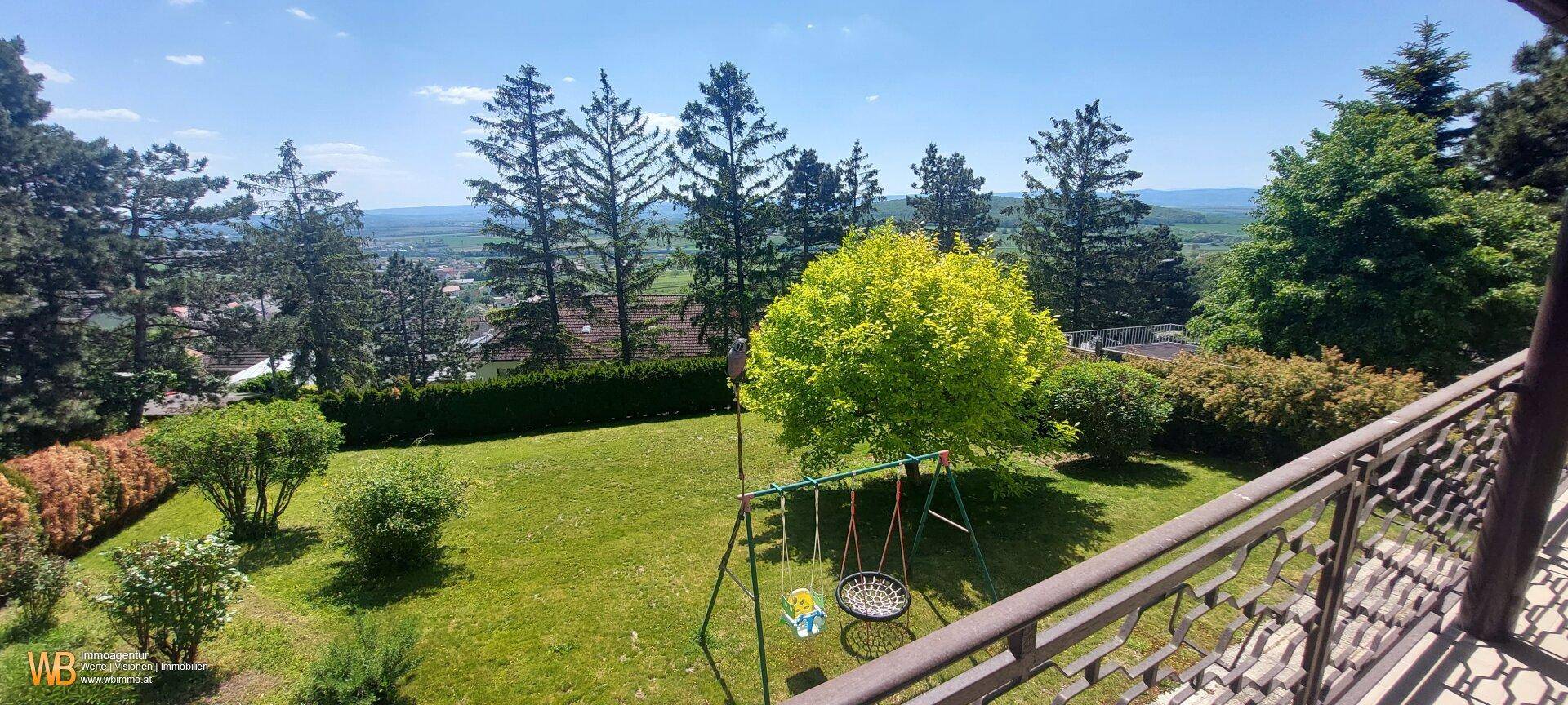 Weitläufiger Blick vom Balkon über den Garten mit Schaukel und die umliegende Landschaft.