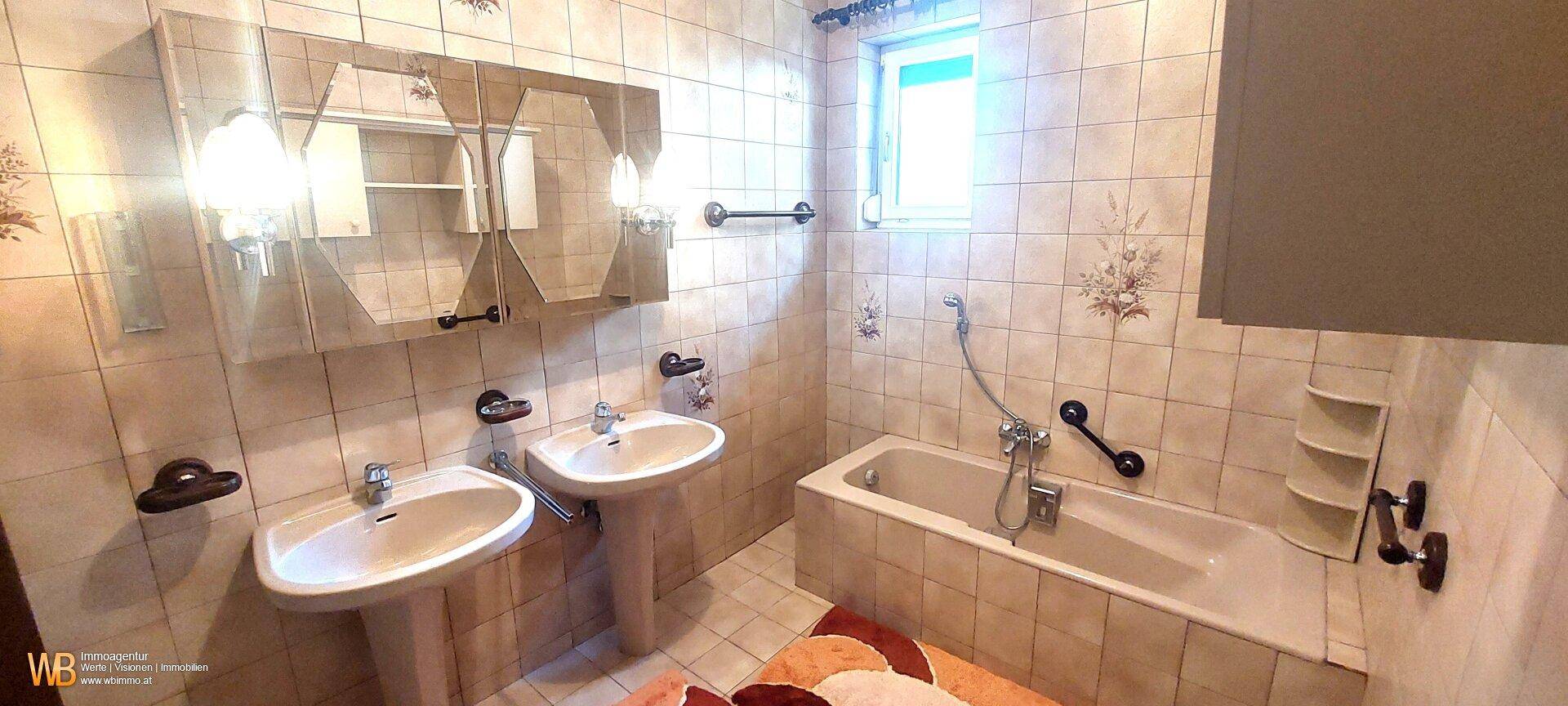 Badezimmer mit zwei Waschbecken, Badewanne und hellen Fliesen an den Wänden.