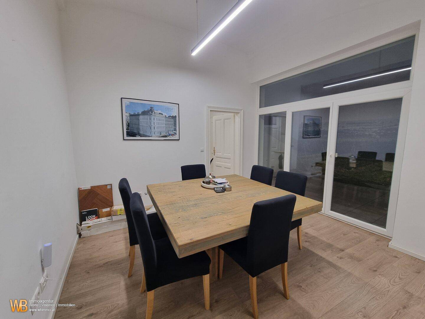 Besprechungsraum mit Holztisch und großen Fenstern, die viel Tageslicht hereinlassen.