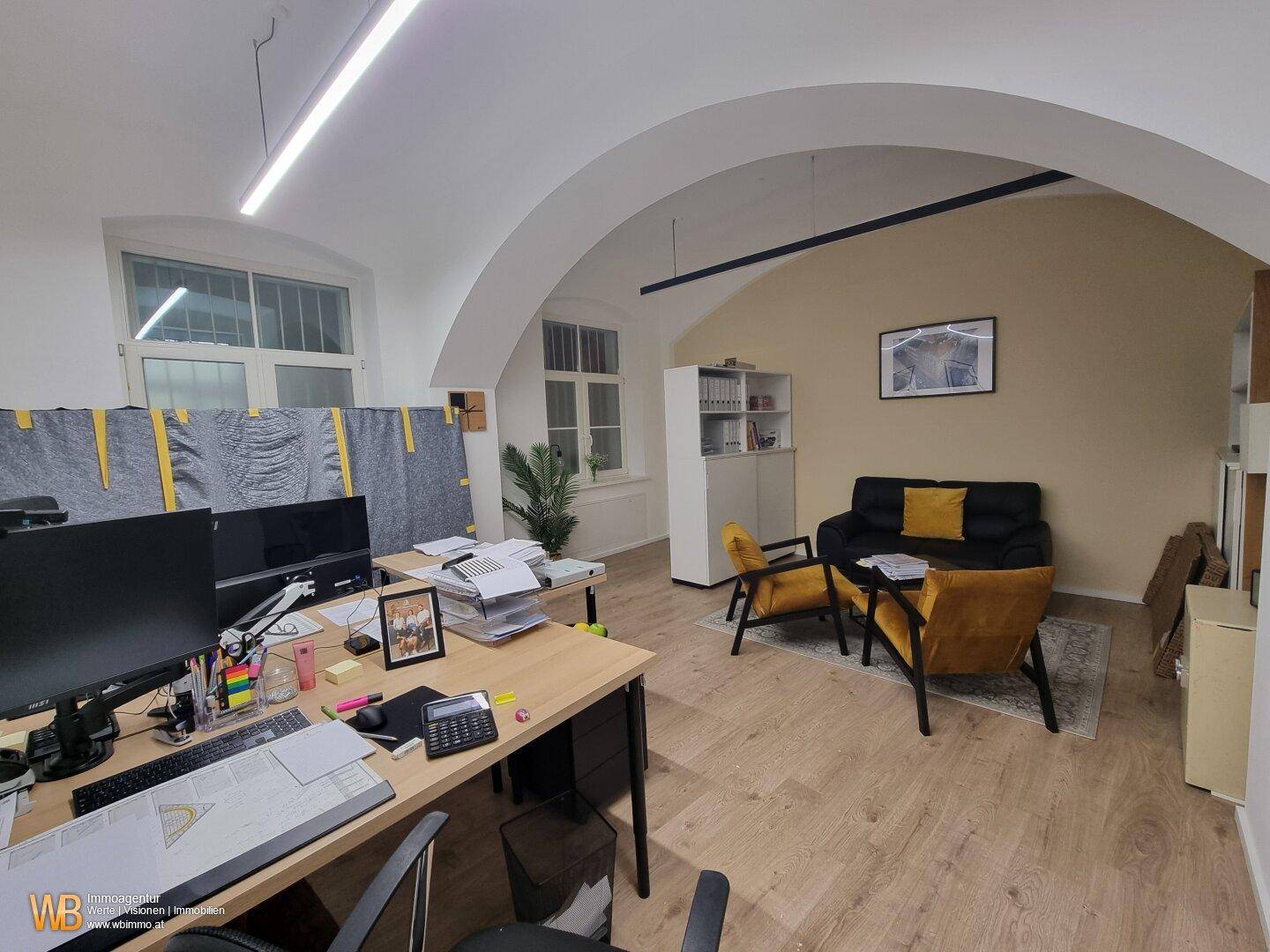 Moderner Bürobereich mit Arbeitsplätzen und einer gemütlichen Sitzecke mit gelben Akzenten.