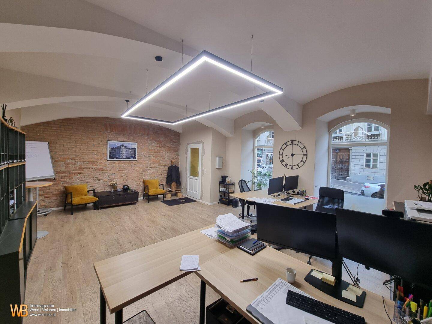 Großzügiges Büro mit mehreren Arbeitsbereichen, Holzboden und Blick auf die Straße.