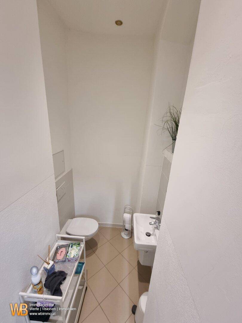 Kompakte Gästetoilette mit WC und kleinem Waschbecken, in neutralen Farbtönen gehalten.