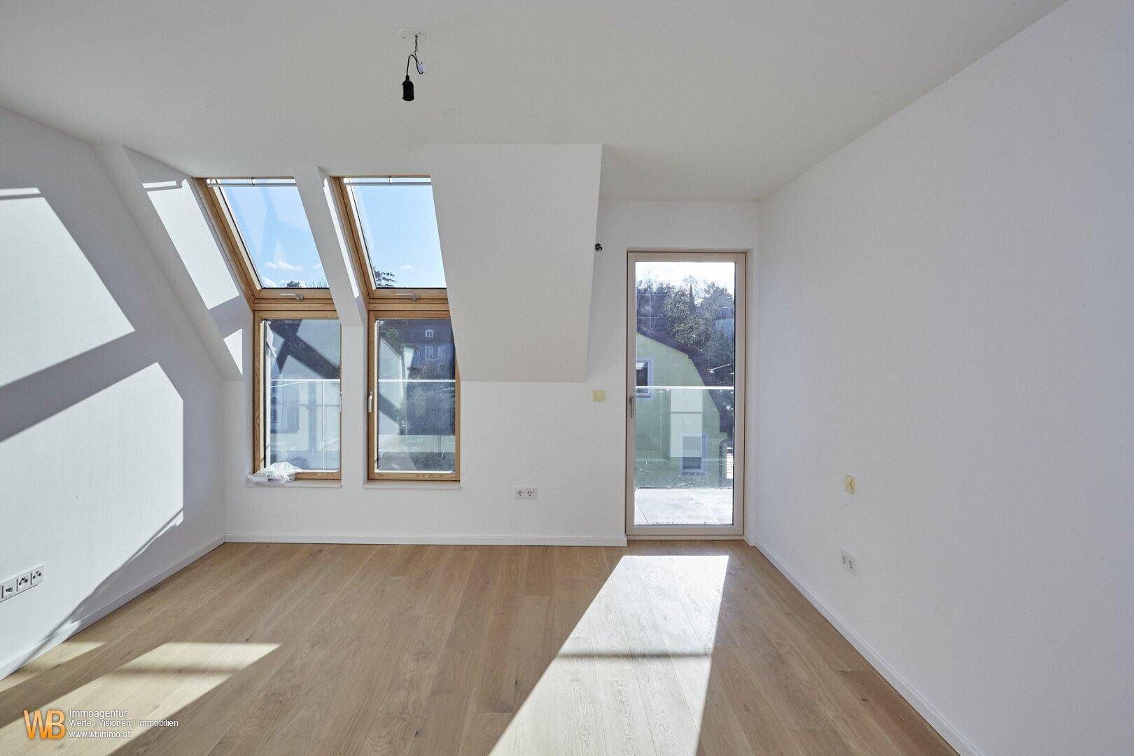 Helles Zimmer mit Holzboden, Dachfenstern und direktem Zugang zu einer Außenterrasse.