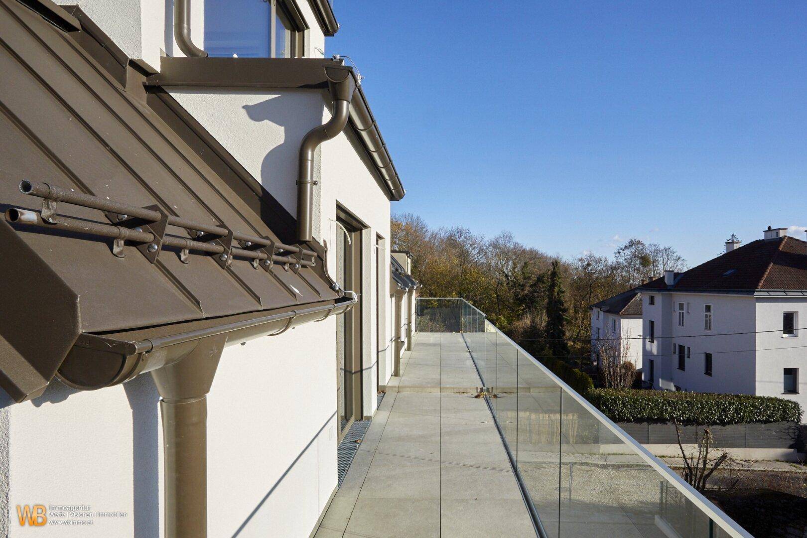 Lange, schmale Terrasse mit Fliesenboden und Glasgeländer bietet einen weiten Blick in die Umgebung.