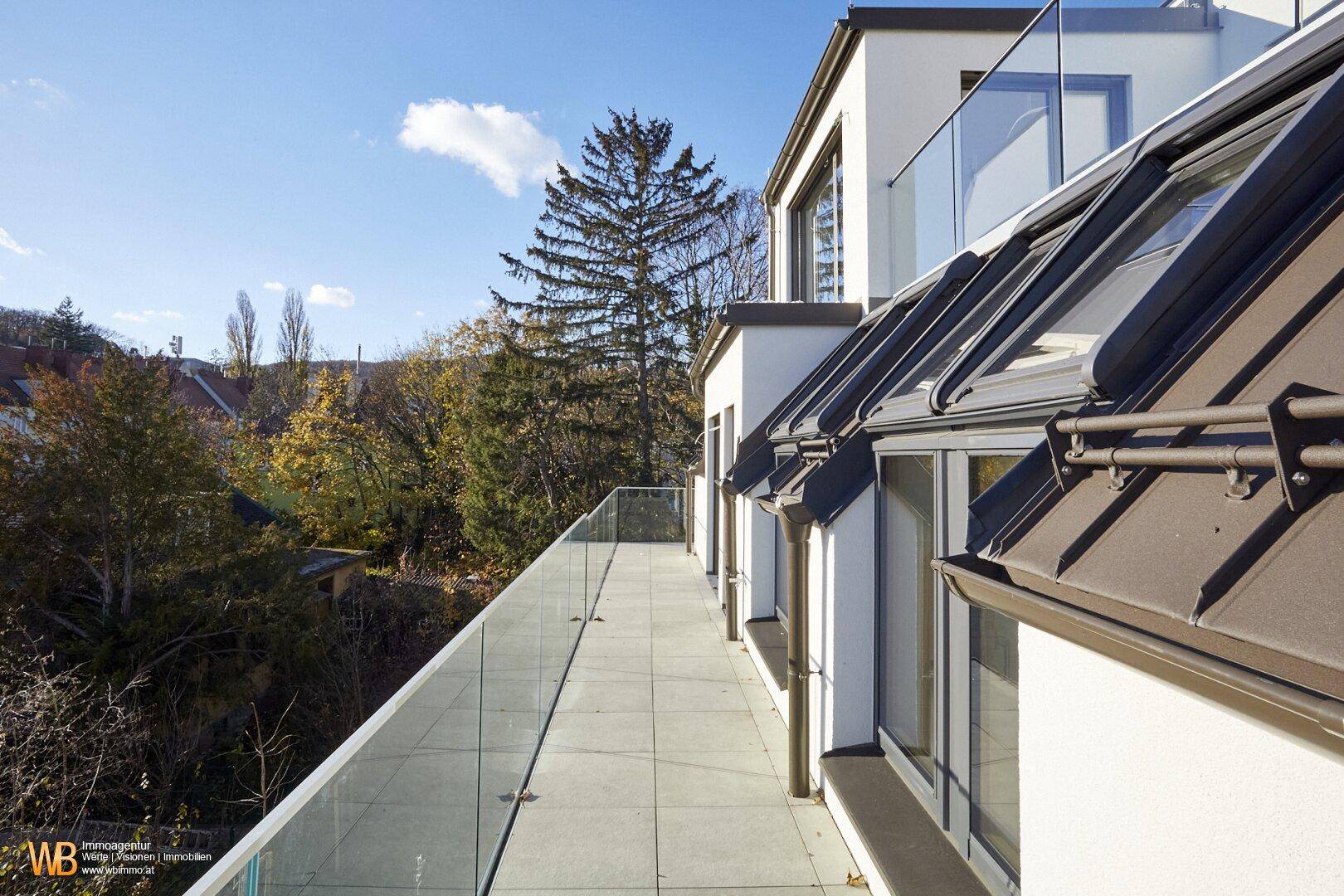 Geräumige Dachterrasse mit Fliesen und Glasbrüstung, umgeben von Bäumen und mit Blick auf die Nachbarschaft.