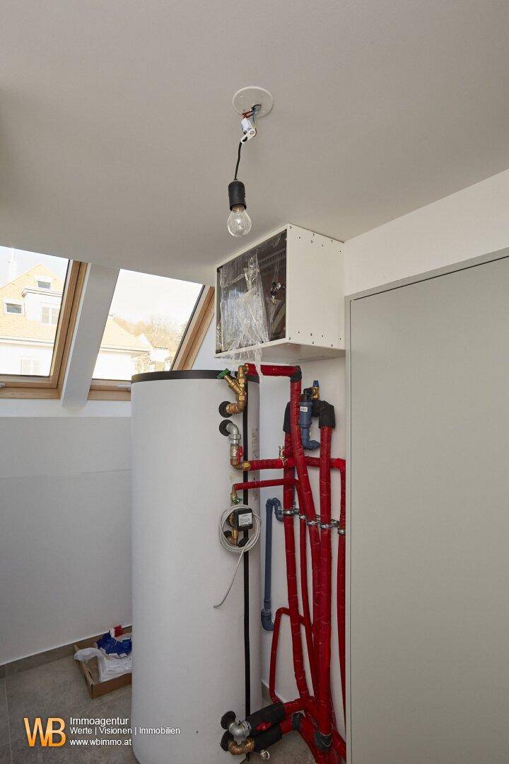 Hauswirtschaftsraum mit großem Warmwasserspeicher, Rohrleitungen und Tageslicht durch Dachfenster.