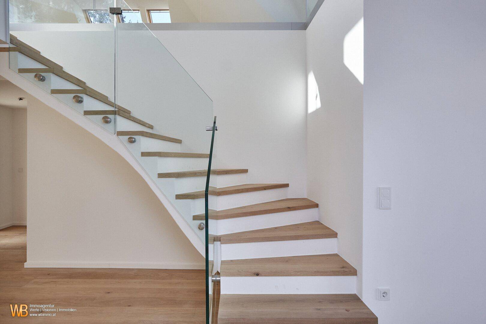 Elegante moderne Treppe mit Holzstufen, weißen Setzstufen und einem stilvollen Glasgeländer.