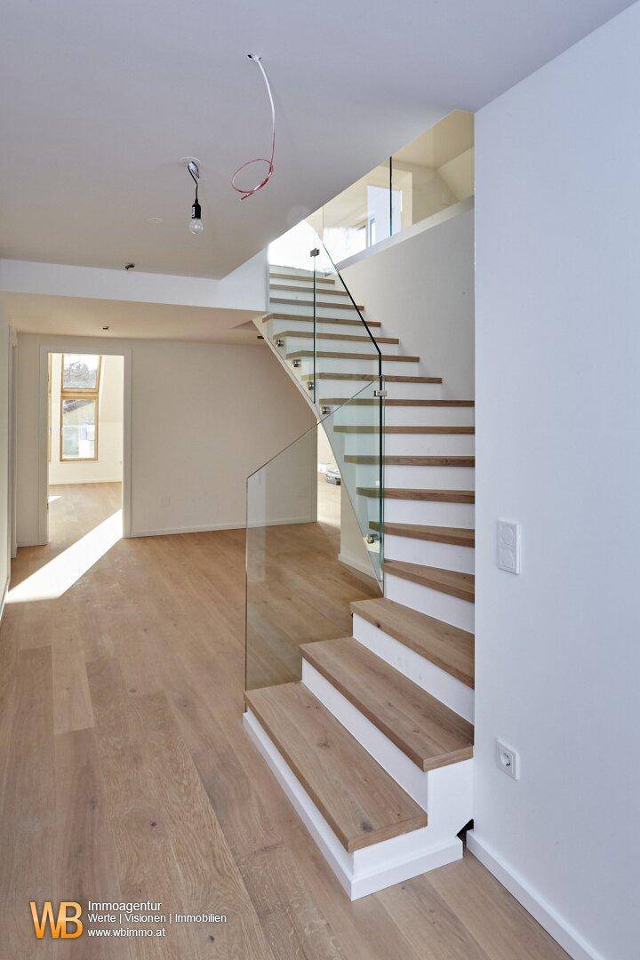 Heller Eingangsbereich mit moderner Holztreppe, Glasgeländer und hellem Parkettboden.