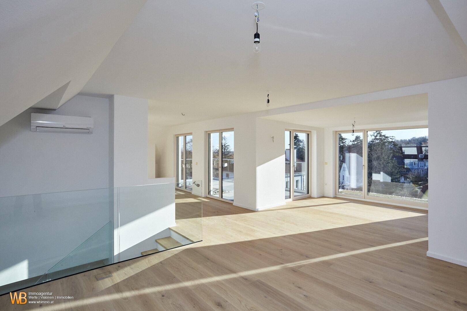 Lichtdurchfluteter Wohnbereich mit hellem Parkettboden, raumhohen Fenstern und Zugang zu einem Balkon.