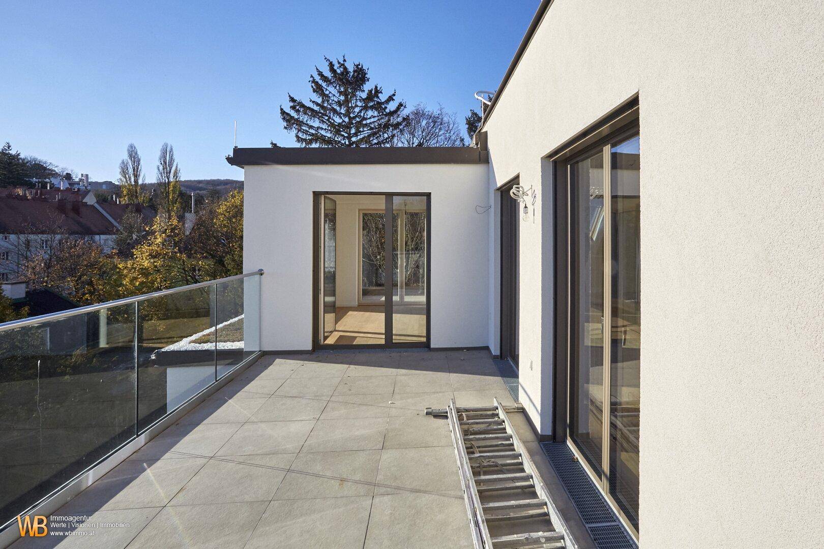 Geräumige Terrasse mit Fliesenboden und Glasgeländer, zugänglich durch große Schiebetüren.
