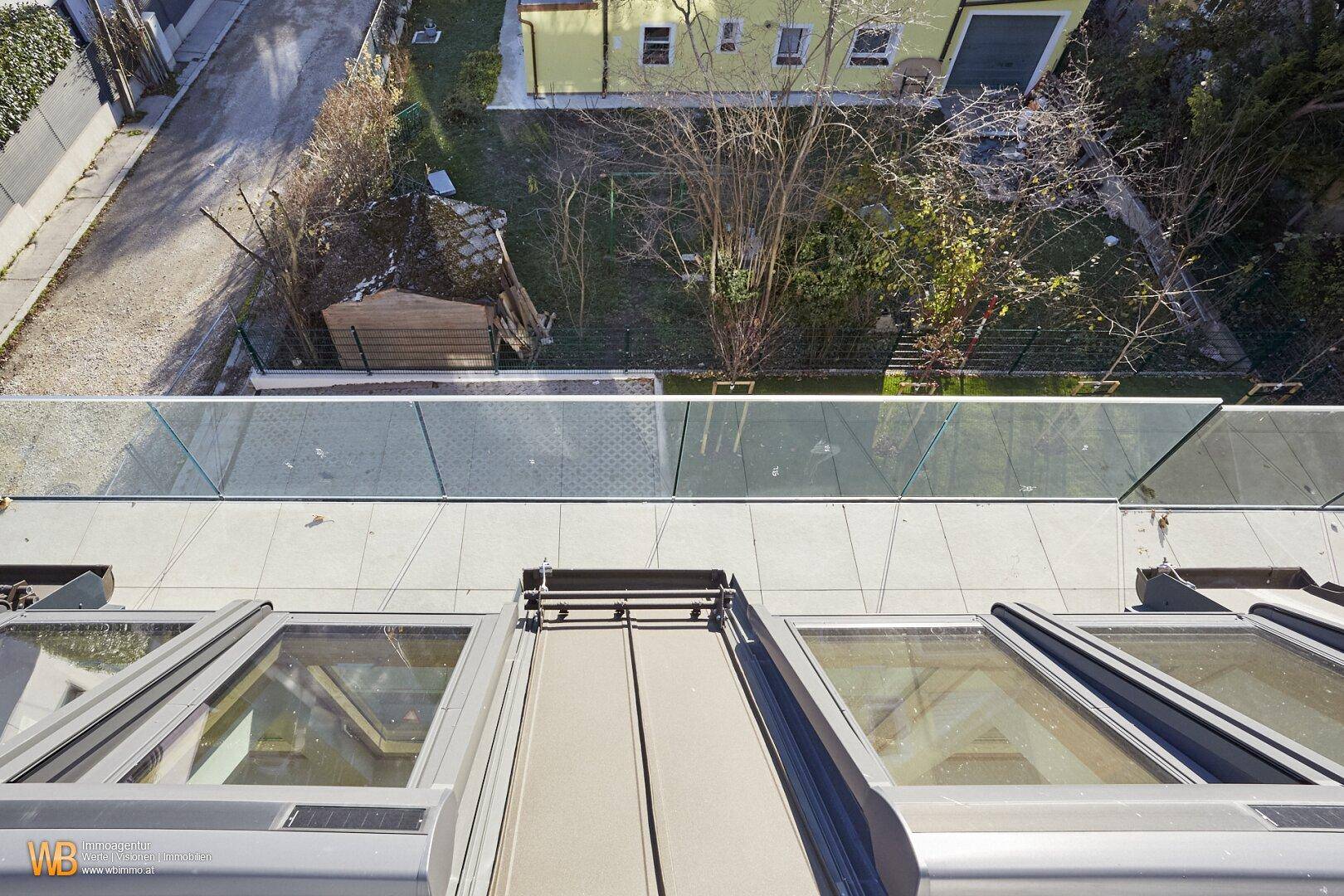 Blick von oben auf die Dachfenster, die geflieste Terrasse und den grünen Gartenbereich.