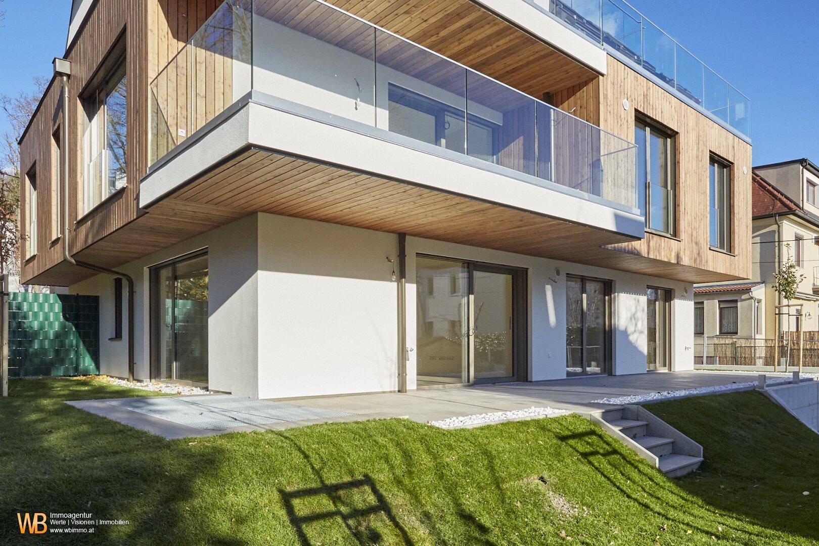 Erdgeschoss mit großen Glasfronten, die zu einer gepflasterten Terrasse und einem kleinen Garten führen.