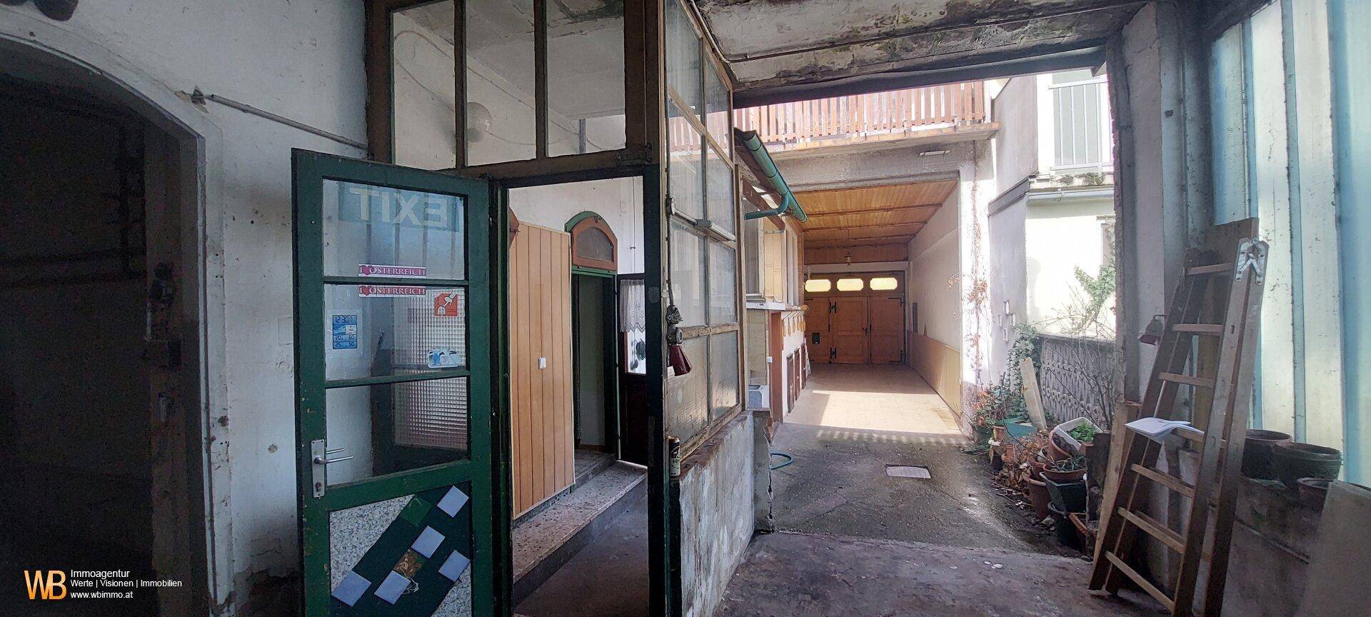 Überdachter Durchgang zu einem Innenhof mit Garagenzugang und alten Holztüren.
