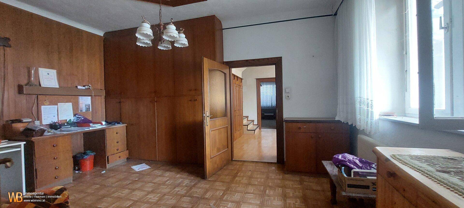 Wohnzimmer mit Holzvertäfelung, Parkettboden und Blick in den Flur.