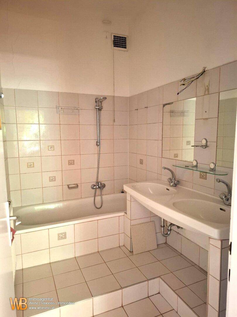 Funktionales Badezimmer mit Badewanne, Doppelsink und Fliesen im Stil der 80er Jahre.