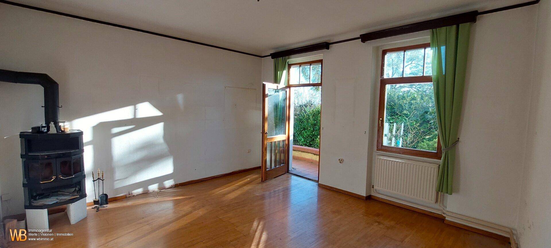 Heller Wohnraum mit Holzboden, gemütlichem Holzofen und Zugang zu einem Außenbereich.