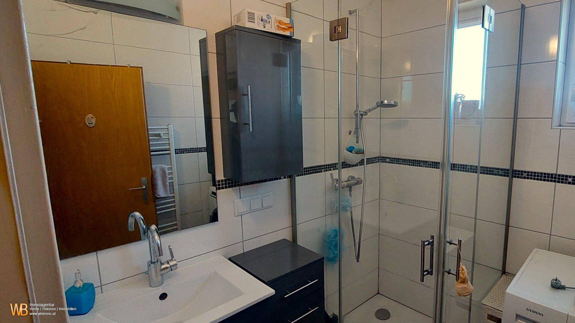 Modernes Badezimmer mit Duschkabine, Waschbecken und beheiztem Handtuchhalter.