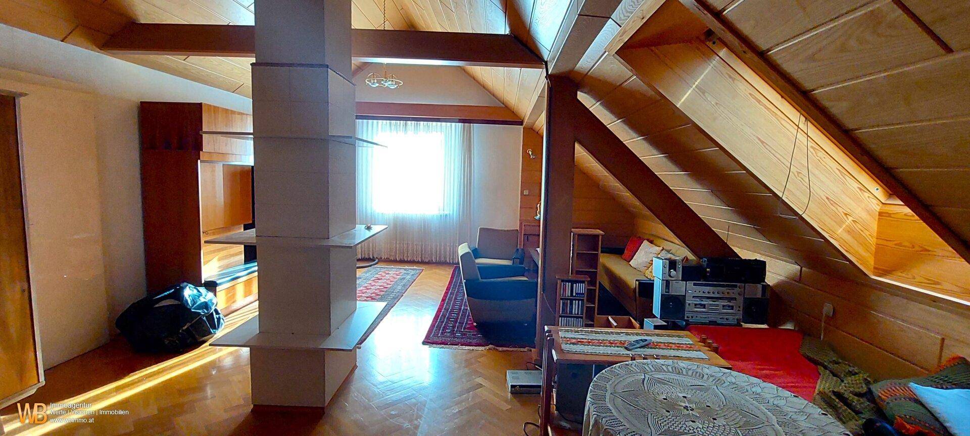 Geräumiger Wohnbereich im Dachgeschoss mit Holzverkleidung, sichtbaren Balken und Dachschrägen.