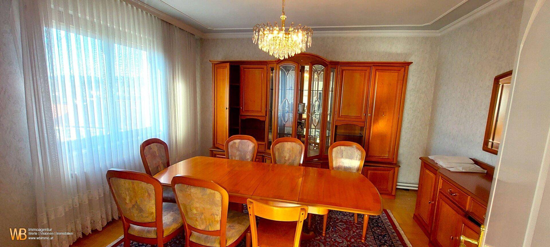 Klassisches Esszimmer mit großem Holztisch, passenden Stühlen und einem eleganten Kronleuchter.