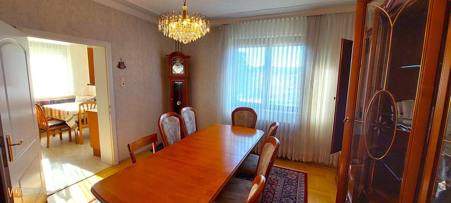 Helles Esszimmer mit einem langen Holztisch, Stühlen und einer traditionellen Standuhr.