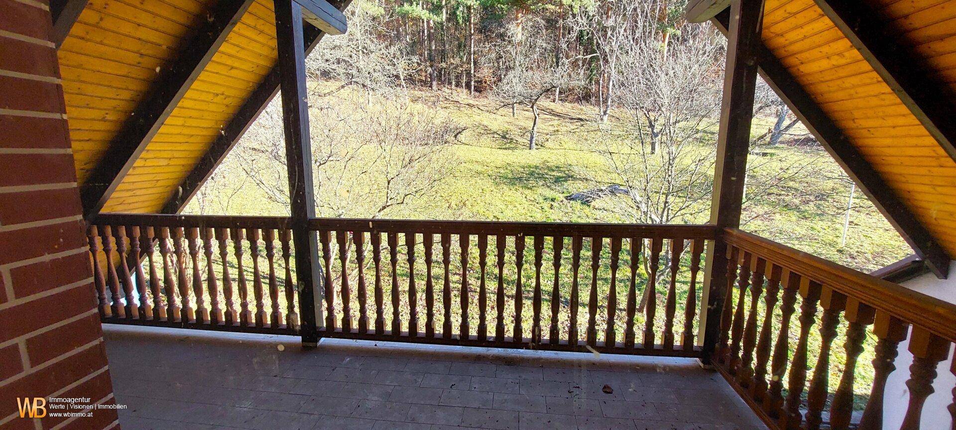 Überdachter Balkon mit Holzgeländer und einem schönen Blick ins Grüne und die umliegende Landschaft.