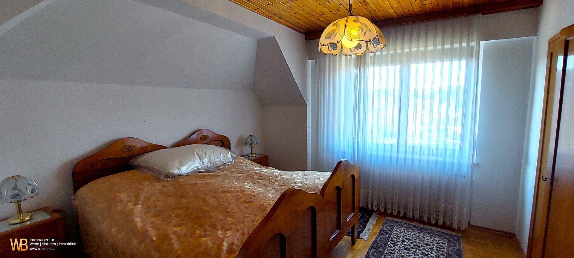 Gemütliches Schlafzimmer im Dachgeschoss mit Holzbett, Teppichboden und einem großen Fenster.