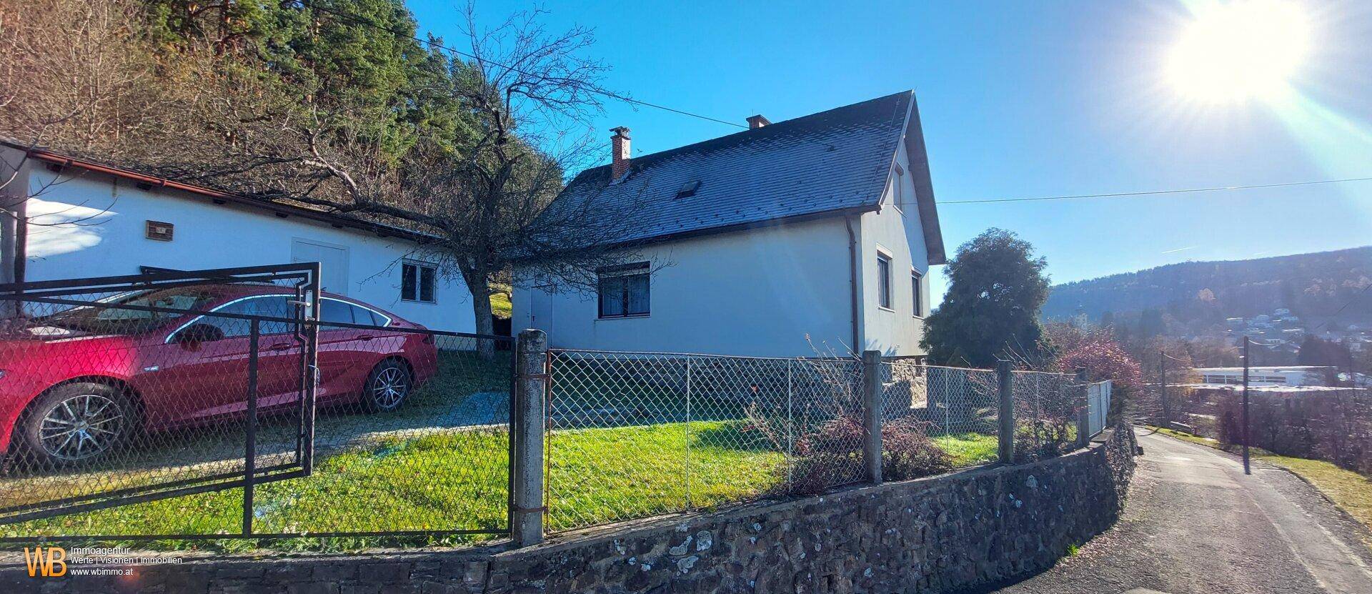 Hausansicht von der Straße mit einem Zaun, einem geparkten Auto und der sonnigen Umgebung.