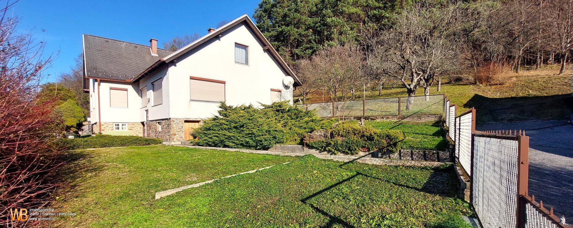 Haus mit einem gepflegten Garten, Rasenflächen und dekorativen Sträuchern in sonniger Lage.
