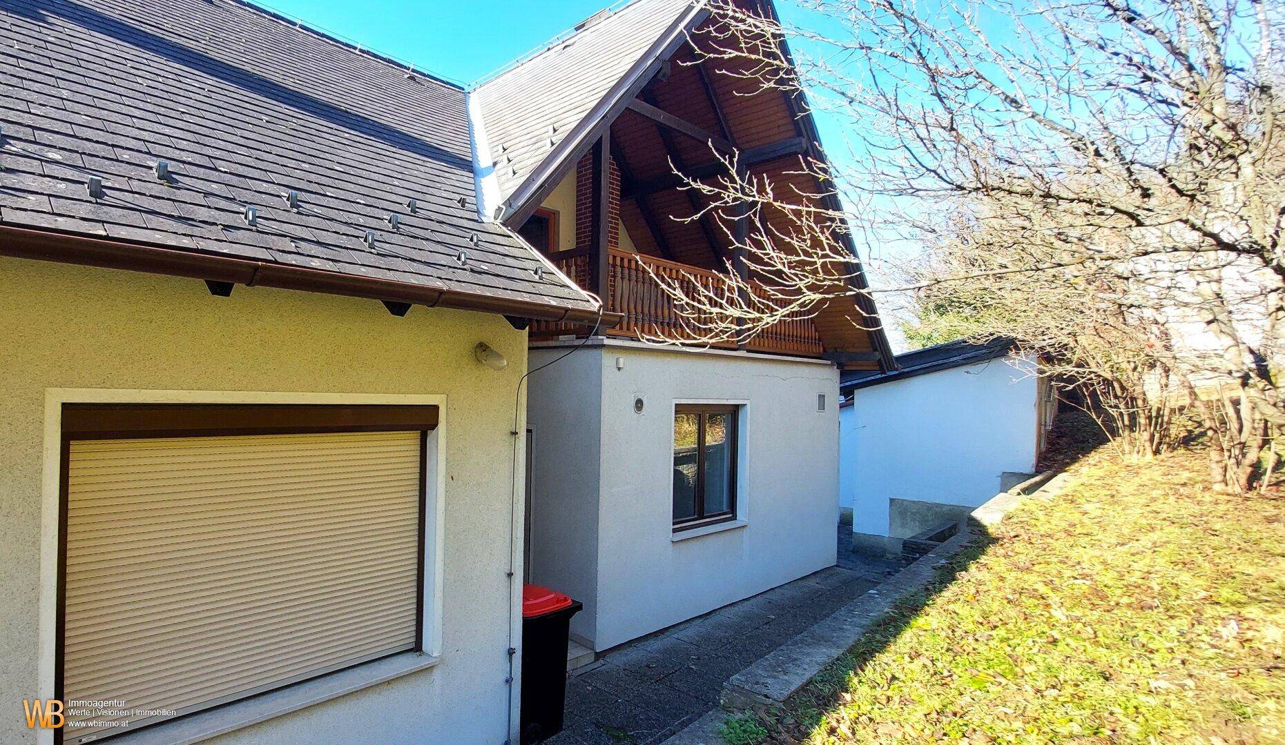 Seitenansicht des Hauses mit einem Balkon, Rollläden und einem angrenzenden Nebengebäude.
