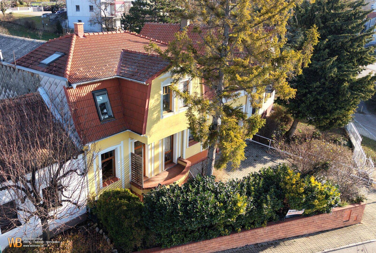 Vogelperspektive des gelben Hauses mit rotem Ziegeldach, umgeben von Bäumen und einem gepflegten Vorgarten.