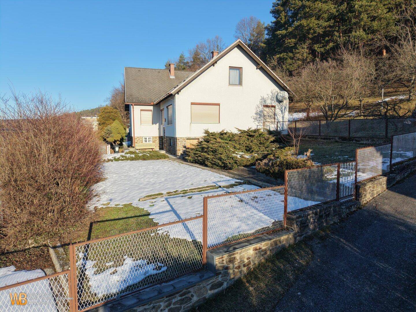 Vogelperspektive auf ein Einfamilienhaus mit Garten, teilweise schneebedeckt, umgeben von Bäumen.