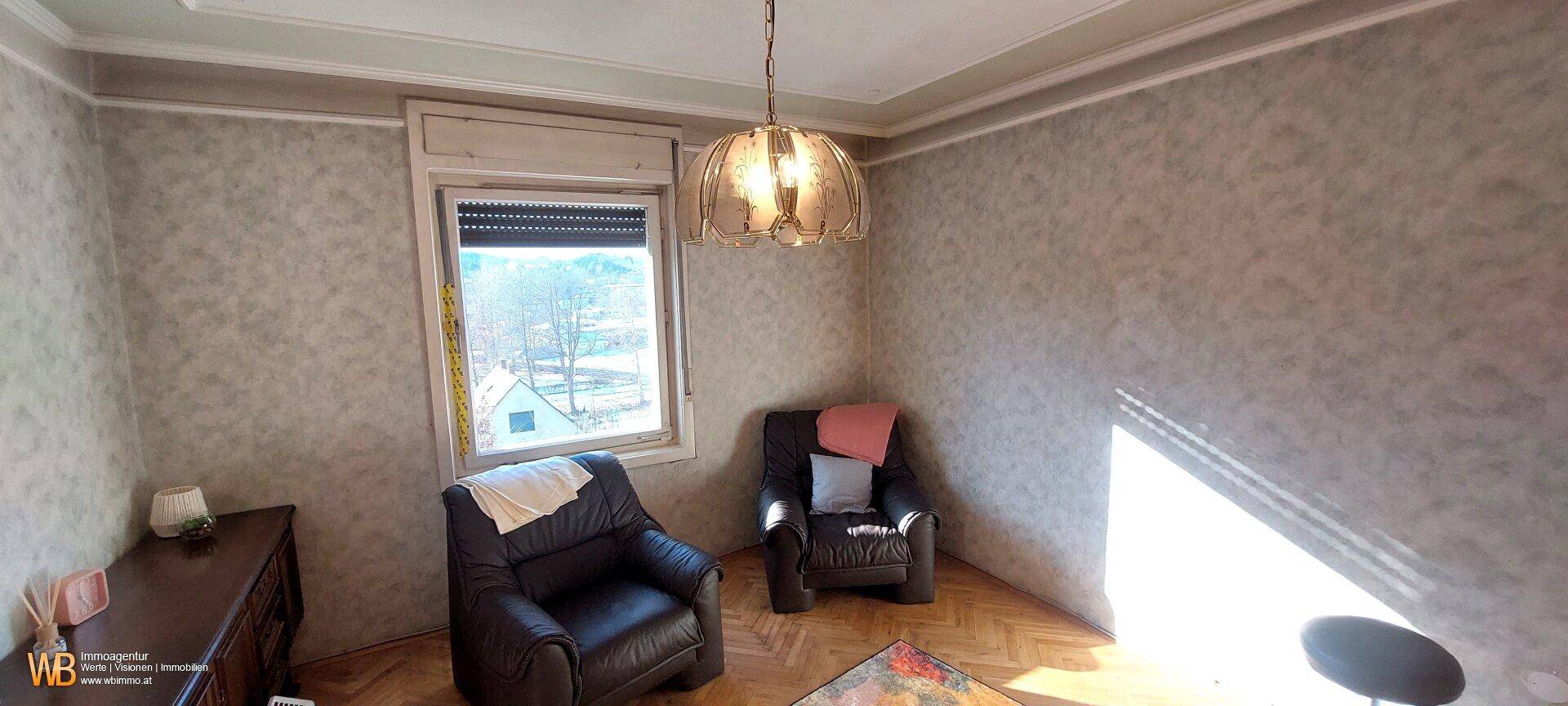 Helles Wohnzimmer mit gemusterter Tapete, Parkettboden und zwei bequemen Sesseln.