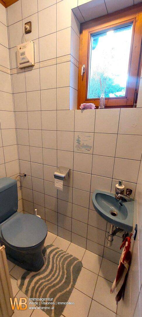 Helles WC mit Fenster, weißen Fliesen und einem kleinen Waschbecken.