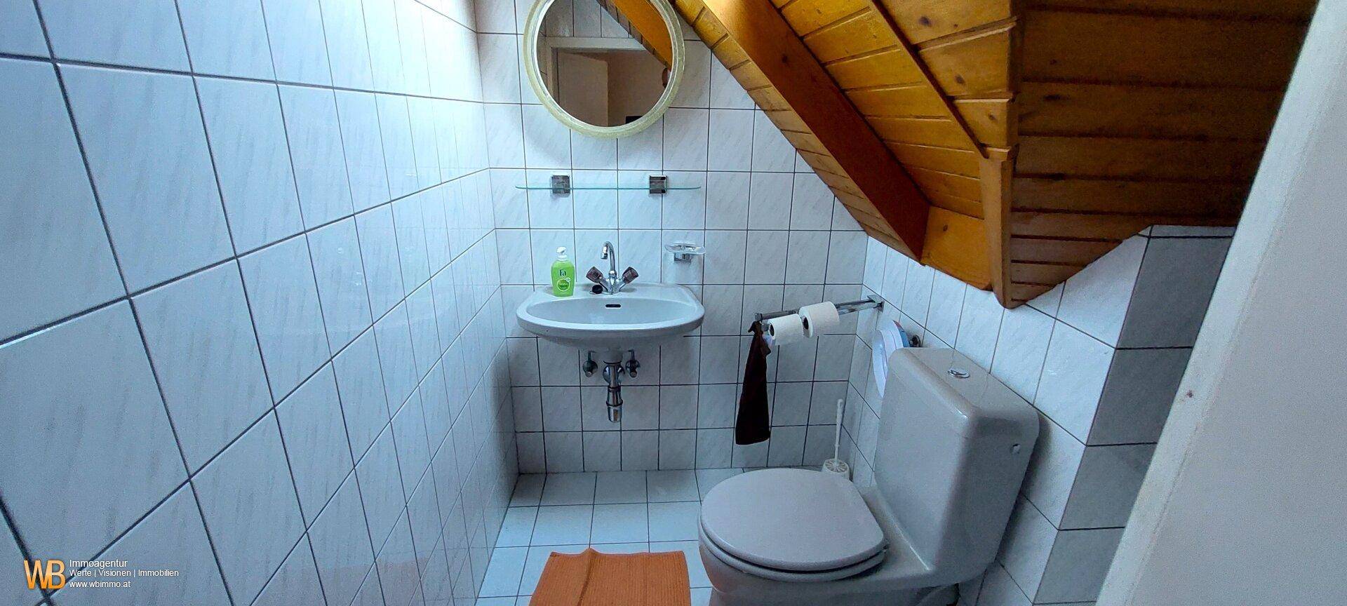 Kleines WC mit weißen Fliesen, Waschbecken und Holzdecke im Dachgeschoss.