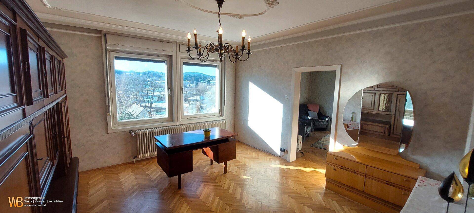 Klassisch eingerichtetes Zimmer mit Parkettboden, Stuckdecke und Blick auf die Umgebung.