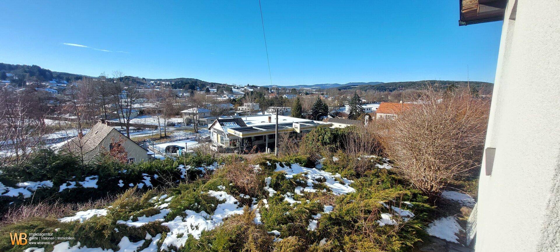 Panoramablick über die verschneite Hügellandschaft und die Dächer der umliegenden Häuser.