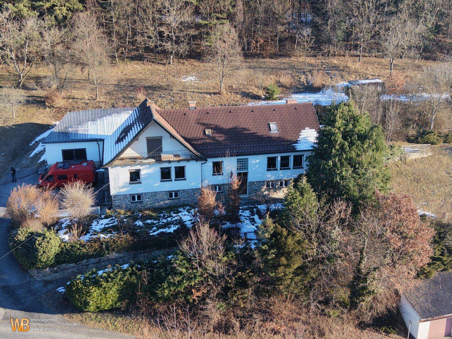 Luftaufnahme des Anwesens mit Hauptgebäude, Nebengebäude und umliegender Natur im Winter.