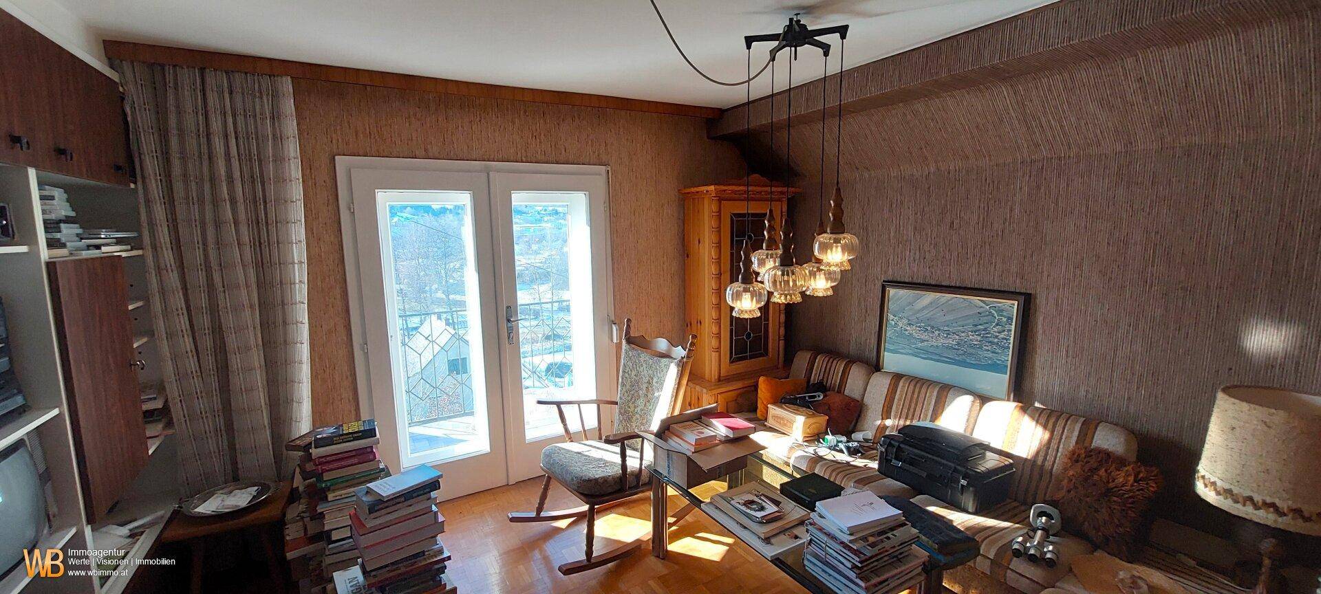 Wohnzimmer mit Holzelementen, gemütlicher Couch und Zugang zu einem Balkon oder einer Terrasse.