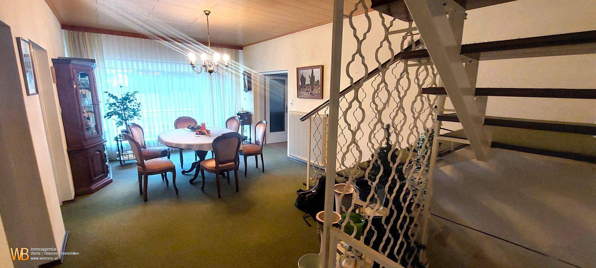 Heller Essbereich mit großem Tisch, Stühlen und Zugang zu einer Treppe.