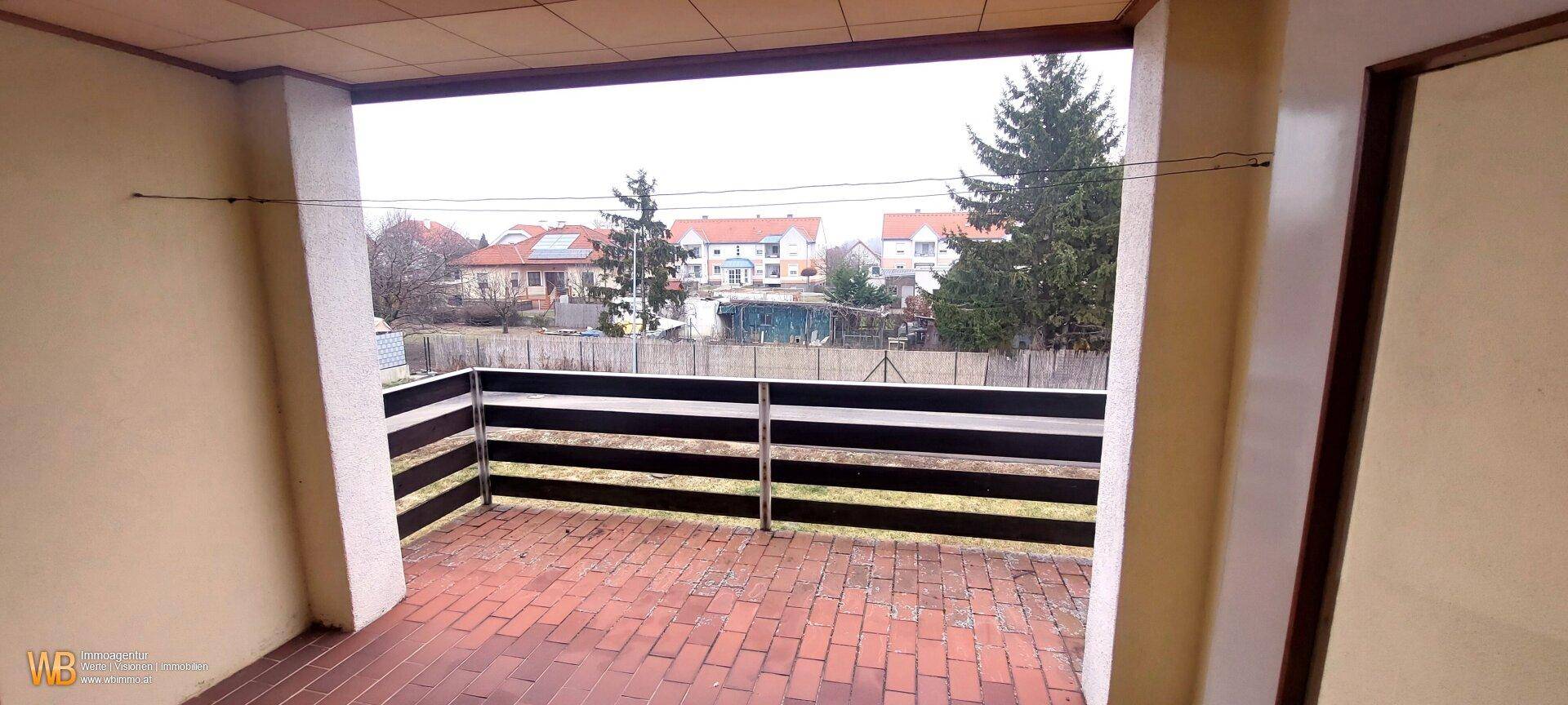 Überdachter Balkon mit Ziegelboden und Blick auf die umliegende Wohnbebauung.