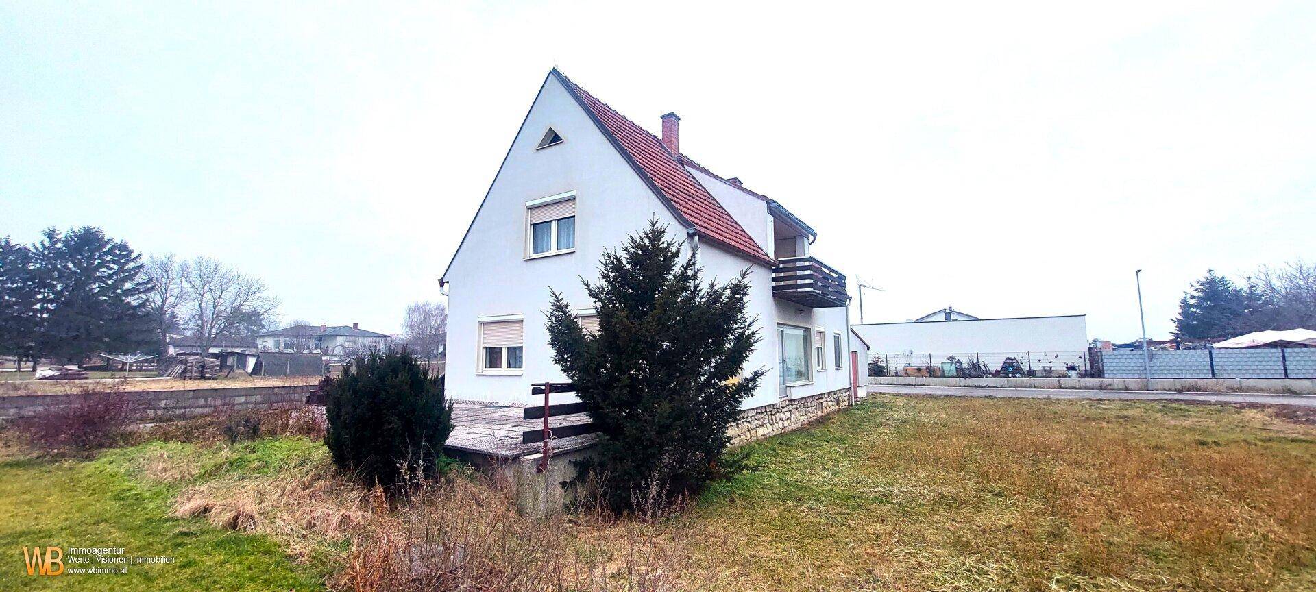 Seitenansicht des Einfamilienhauses mit Balkon und weitläufigem, grünem Grundstück.