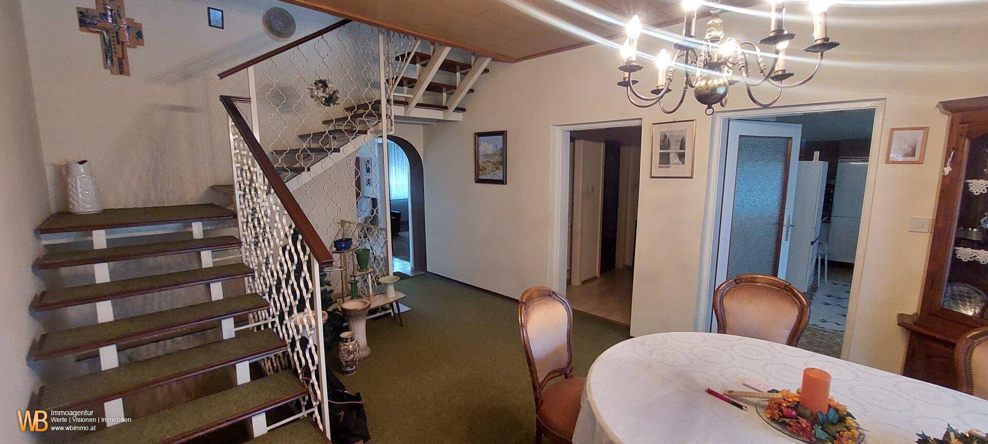 Geräumiger Flur mit einer Holztreppe, Teppichboden und einem Kronleuchter.