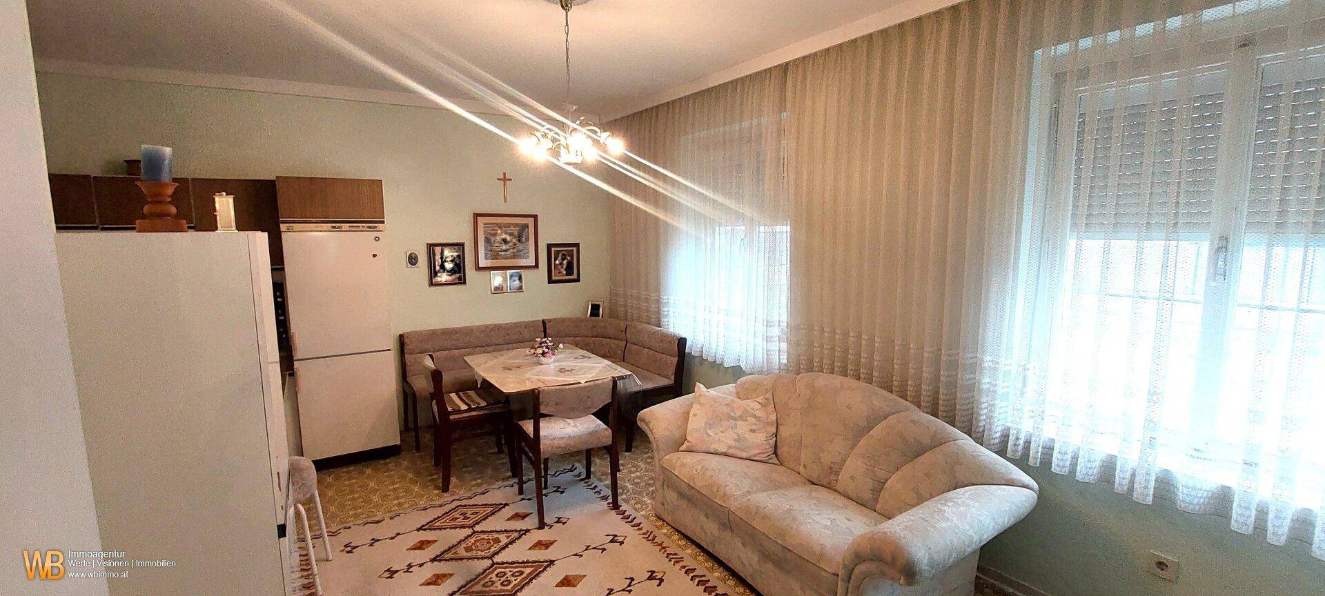 Gemütlicher Wohnbereich mit Sofa, Esstisch und Blick auf die Fenster mit Vorhängen.