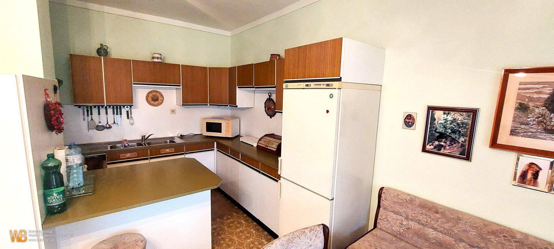 Funktionale Küche mit Holzfronten, integrierten Geräten und einem kleinen Essbereich.