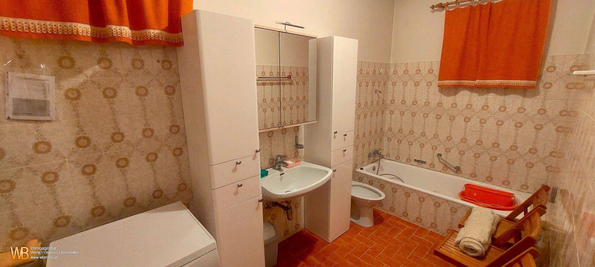 Funktionales Badezimmer mit Badewanne, Waschbecken und gemusterten Fliesen.