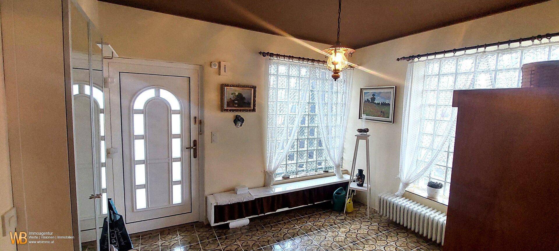 Heller Eingangsbereich mit Fliesenboden, Glasbausteinfenstern und einer dekorativen Deckenleuchte.