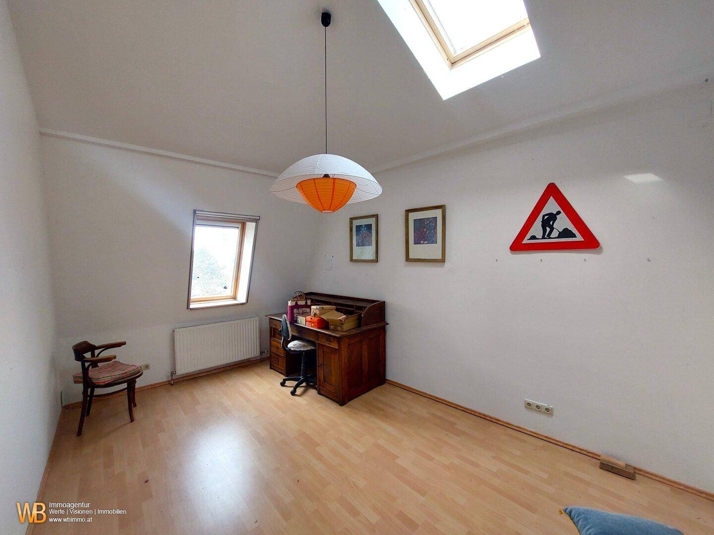 Helles Dachzimmer mit Schreibtisch, Holzboden und Dachfenstern, ideal als Arbeitsbereich.