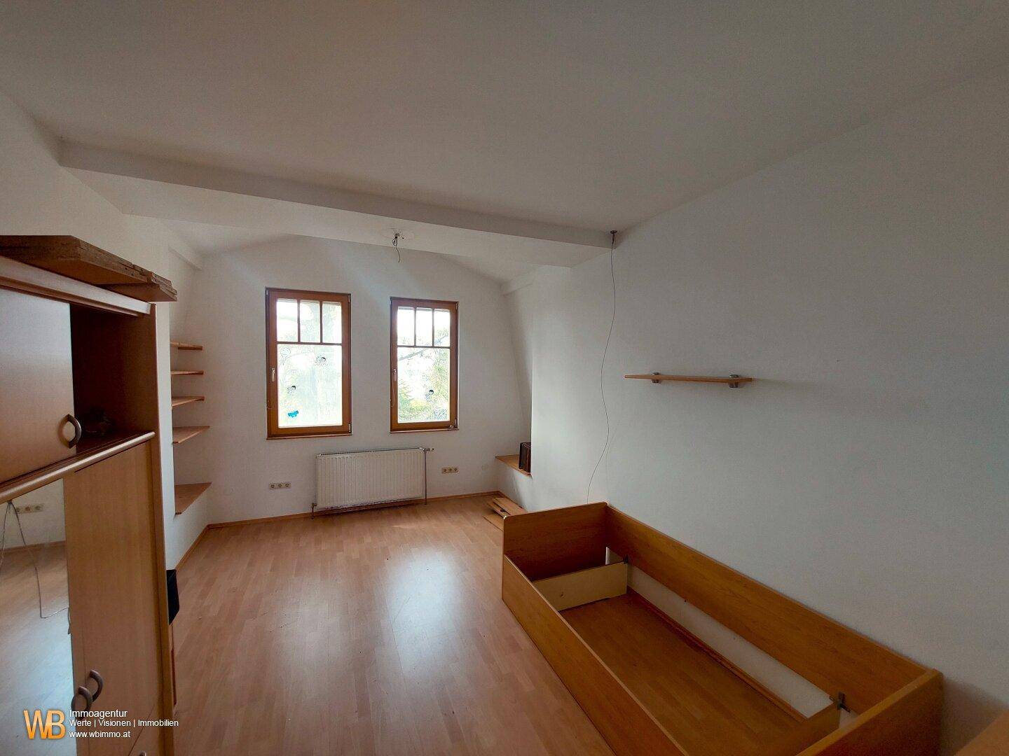 Helles Schlafzimmer mit Holzboden, zwei Fenstern und Dachschräge, gemütlich und funktional.